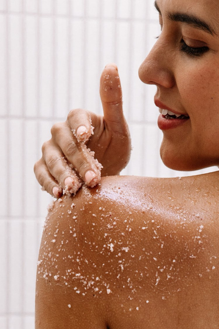 Person applying a scrub to their shoulder with a smile.