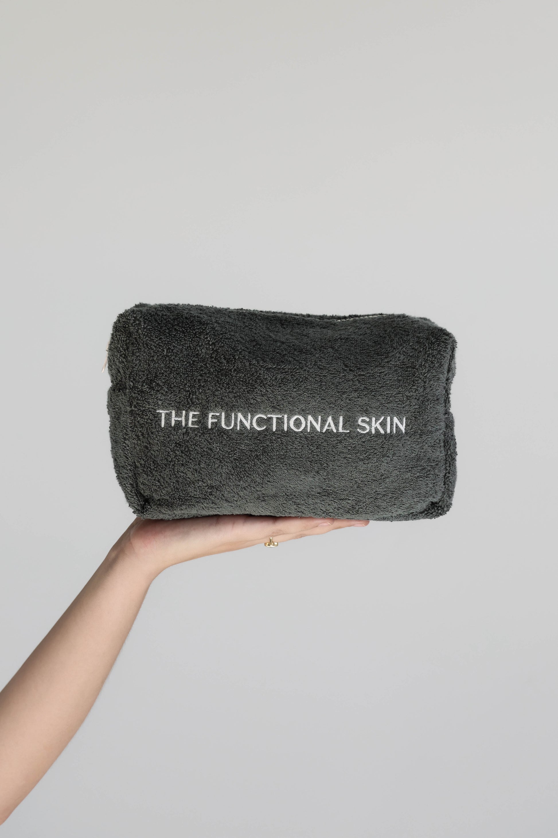 A hand holding a gray terry towelling bag with 'THE FUNCTIONAL SKIN' printed on it.