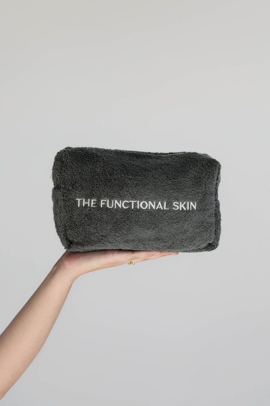 A hand holding a gray terry towelling bag with 'THE FUNCTIONAL SKIN' printed on it.