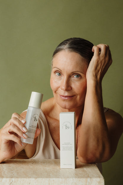 Woman holding The Audrey Age Renewal Mist against a green background