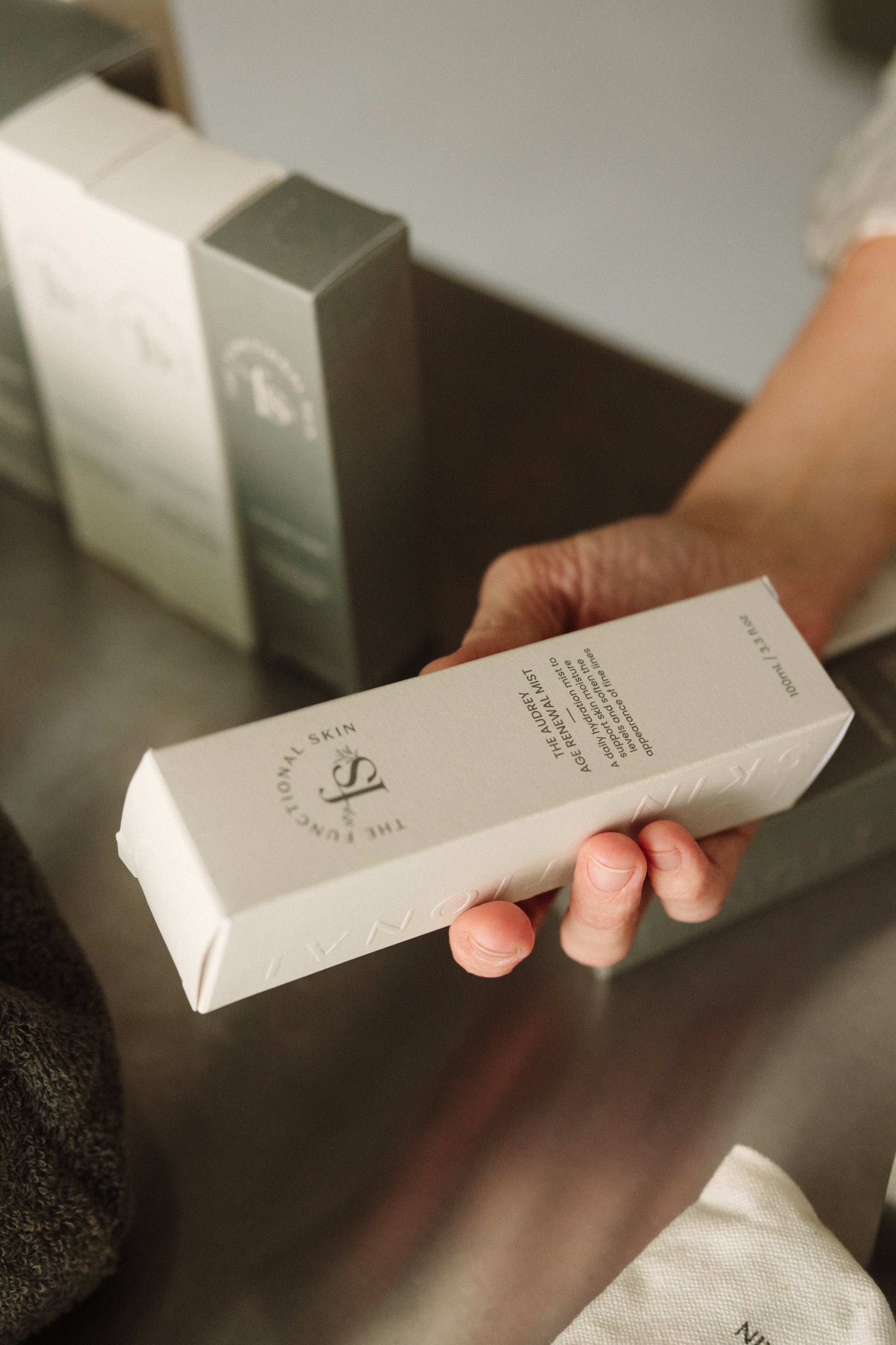 Person holding The Audrey Age Renewal Mist on a blurred background