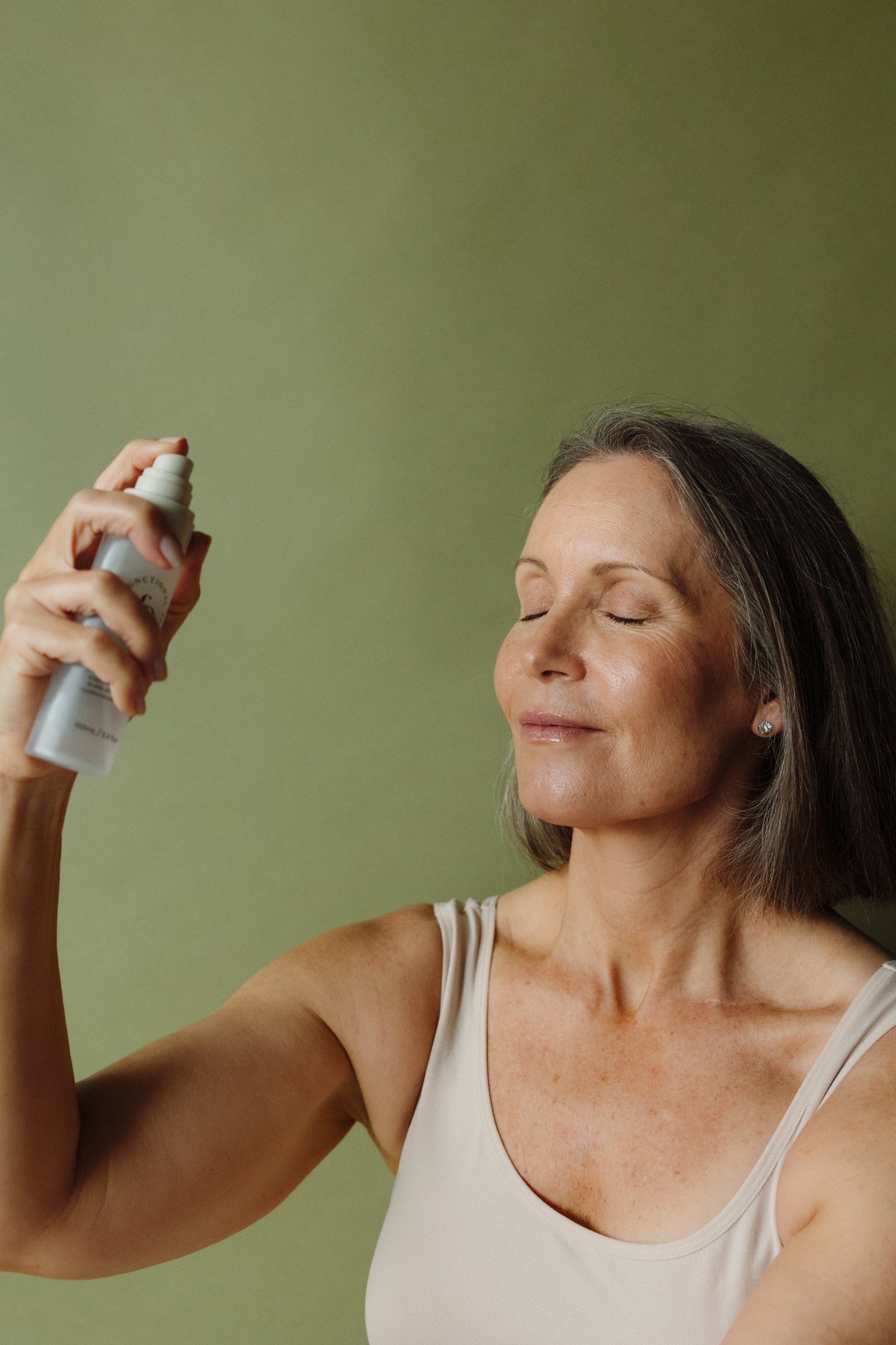 Woman applying a spray to her face against a green background