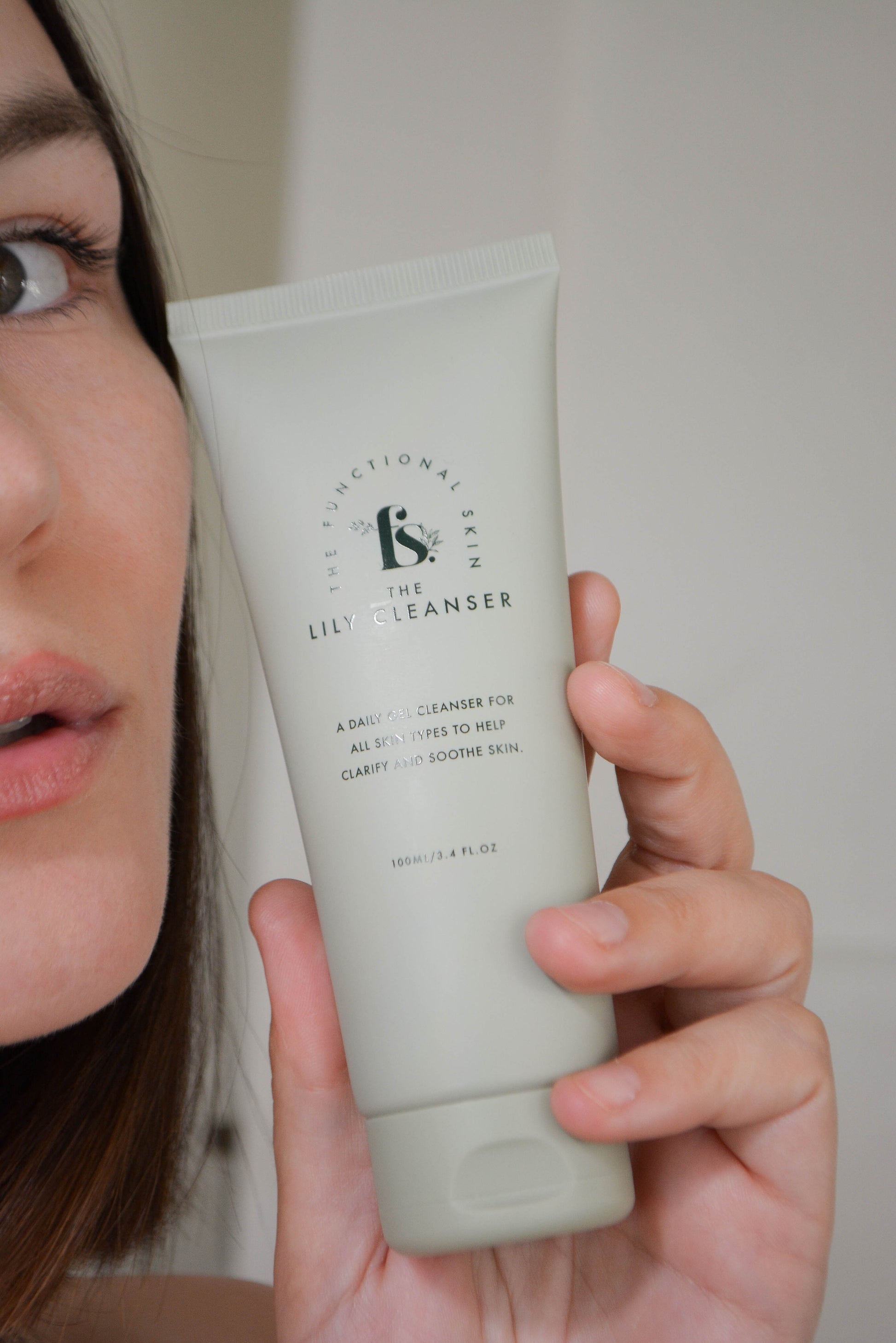 Bottle of the Lily Cleanser in front of a women's face in hand 